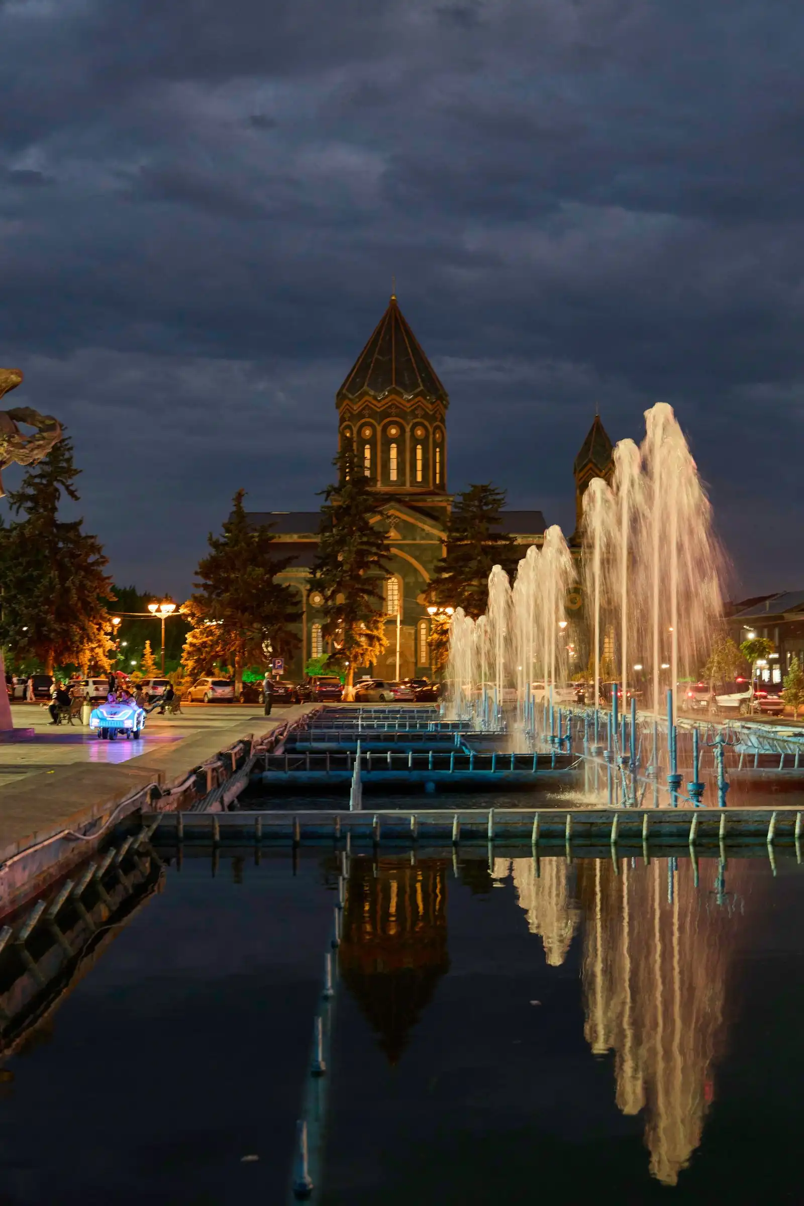 An illuminated church and fountain in Gyumri at twilight