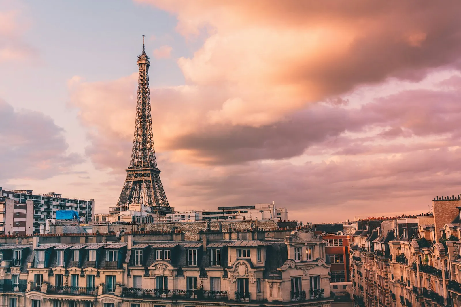 The Eiffel Tower above Paris rooftops beneath a pink evening sky