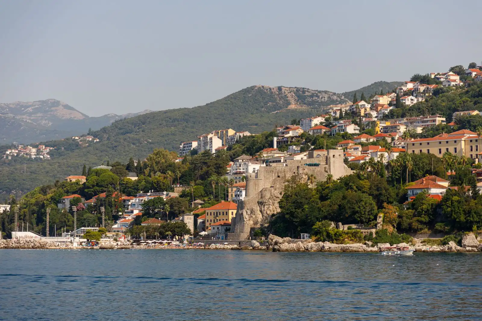 Herceg Novi's waterfront and stone fortress below green hills