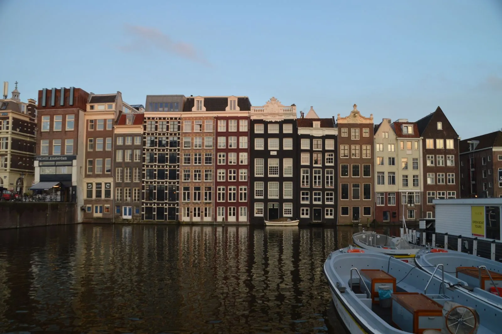 Amsterdam canal houses reflected in the water, with moored boats in the foreground