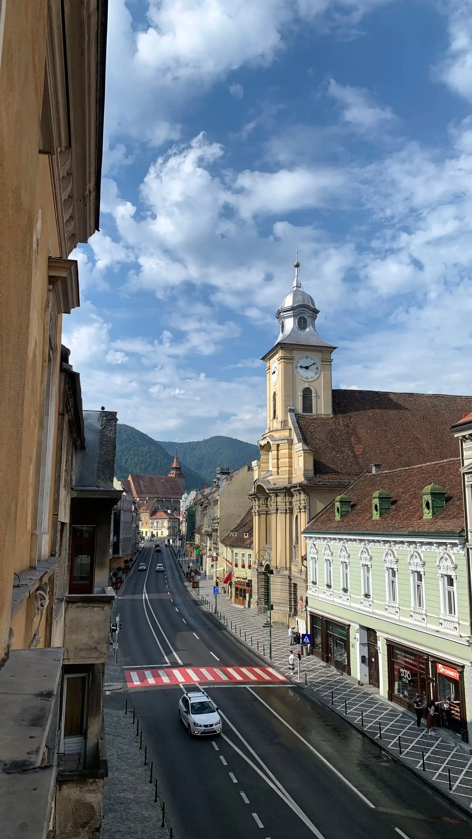 A church tower and historic buildings along a street in Brașov