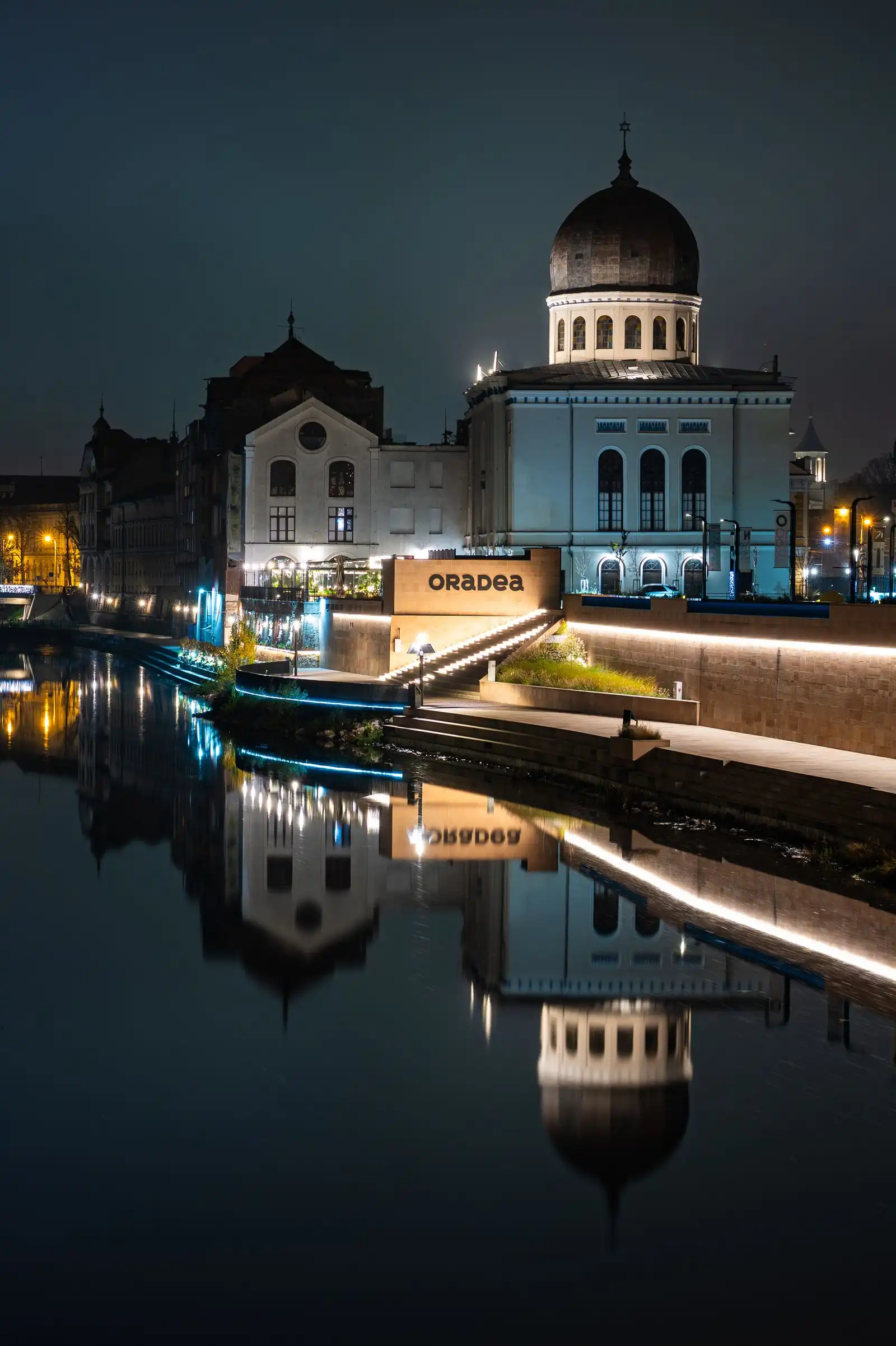 An illuminated domed building beside the river in Oradea