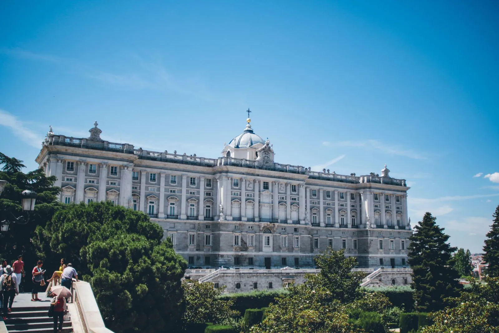 Royal Palace of Madrid seen above trees and gardens beneath a blue sky