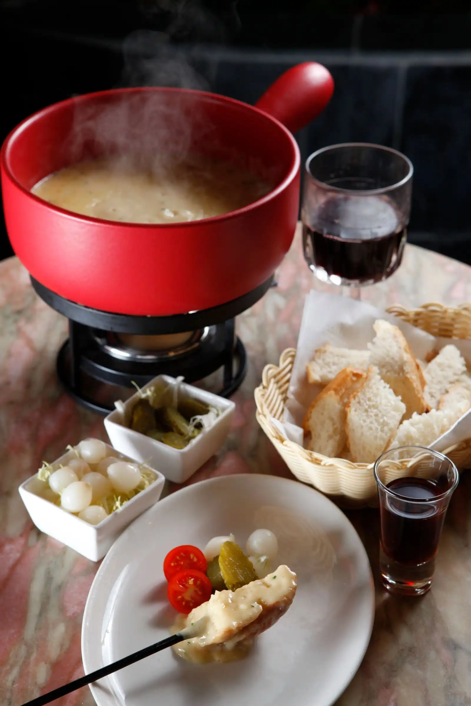 A pot of cheese fondue served with bread and pickles