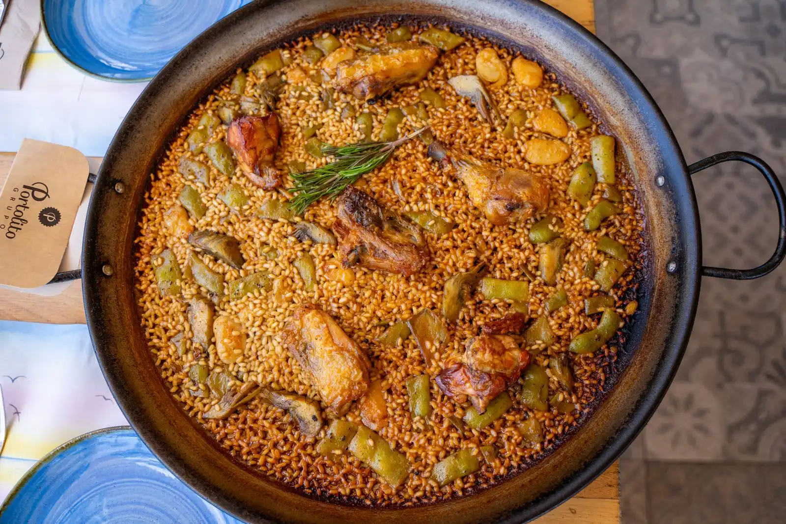 A pan of paella with chicken, vegetables and rosemary