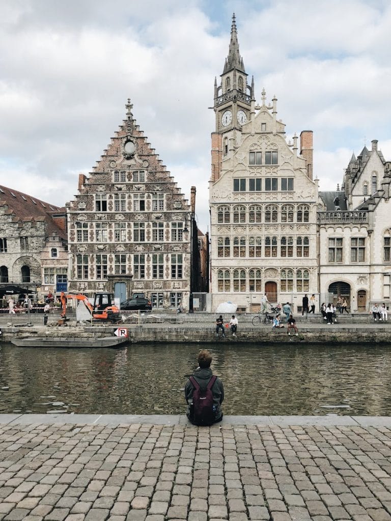 Person sitting by Ghent canal in Belgium, with view of historic architecture.